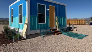 A small, single-story building with a blue and white exterior, a door, and windows. - Charming Desert Beach House Tiny home, with AC, WiFi, game room/fitness room. (Beryl)