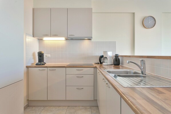 Una cocina moderna con gabinetes de color claro, un lavamanos de acero inoxidable y una cafetera.