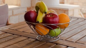 Una cesta de frutas sobre una mesa de madera, con paredes de piedra al fondo.
