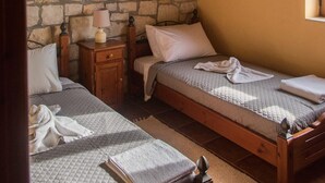 Una habitación con dos camas de madera, una pared de piedra, techo de madera y una pequeña mesa con lámpara.