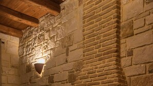 Una chimenea de piedra con fuego, un sillón de mimbre y un muro de piedra.