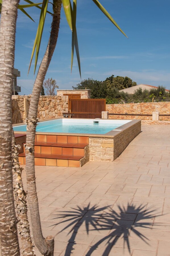 A swimming pool with stone walls and wooden steps, surrounded by palm trees and a stone wall. - Ydria Villa A With Pool (Hersonissos)