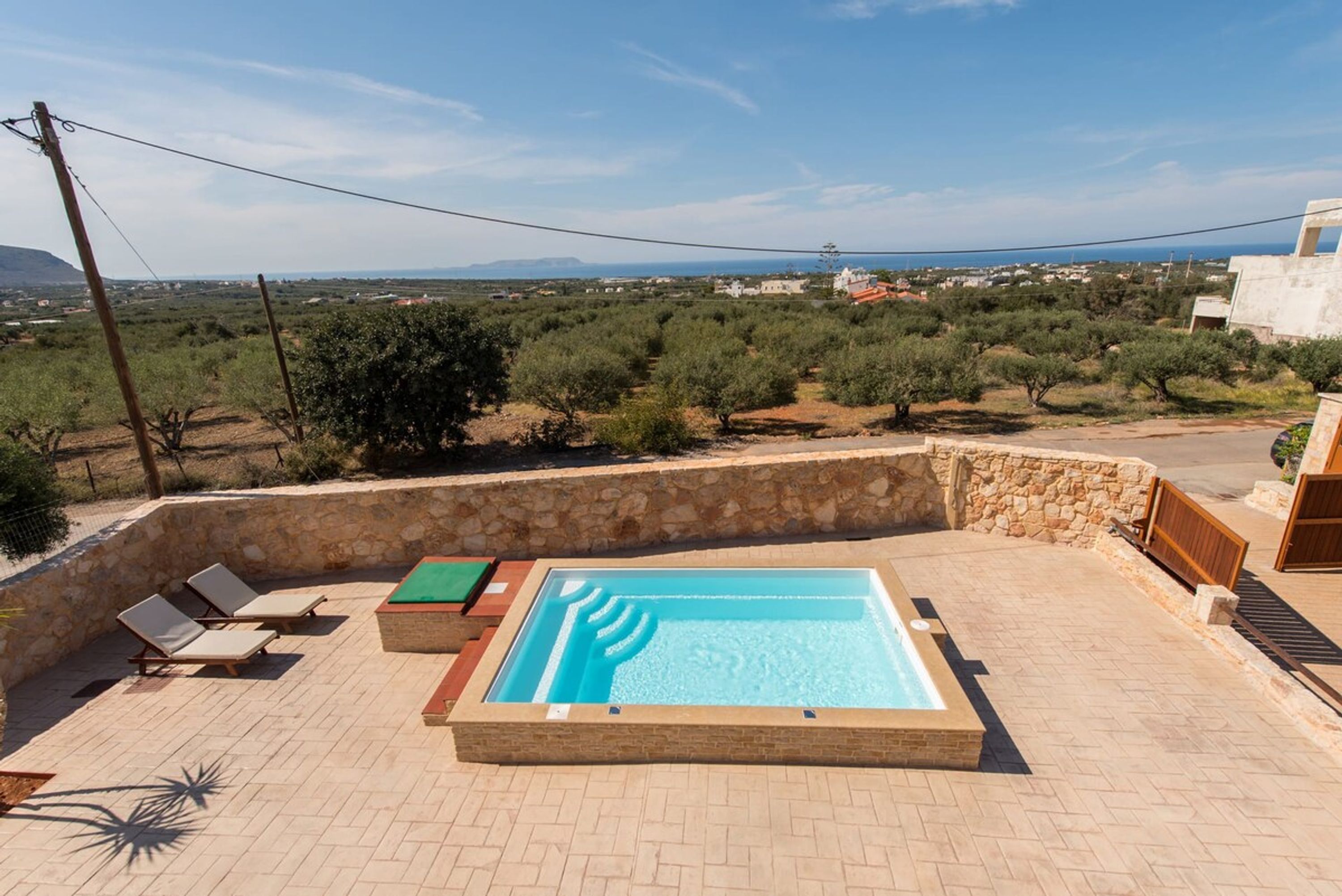 A rooftop swimming pool with a stone wall, lounge chairs, and a view of the countryside.