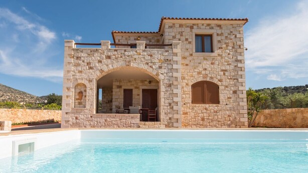 Una villa de piedra con piscina, que cuenta con un arco de piedra en la entrada y una terraza.