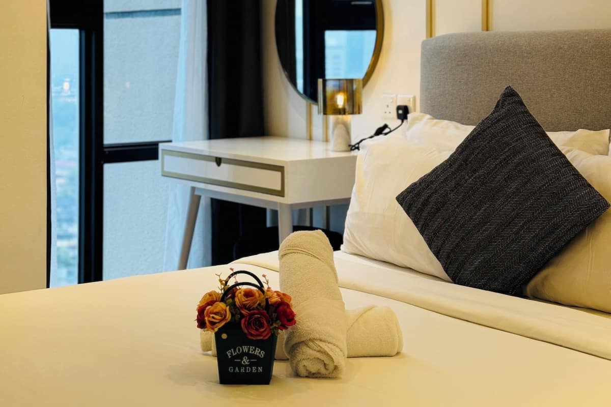 A hotel room with a bed, a bedside table, a mirror, a window, and a bouquet of flowers.