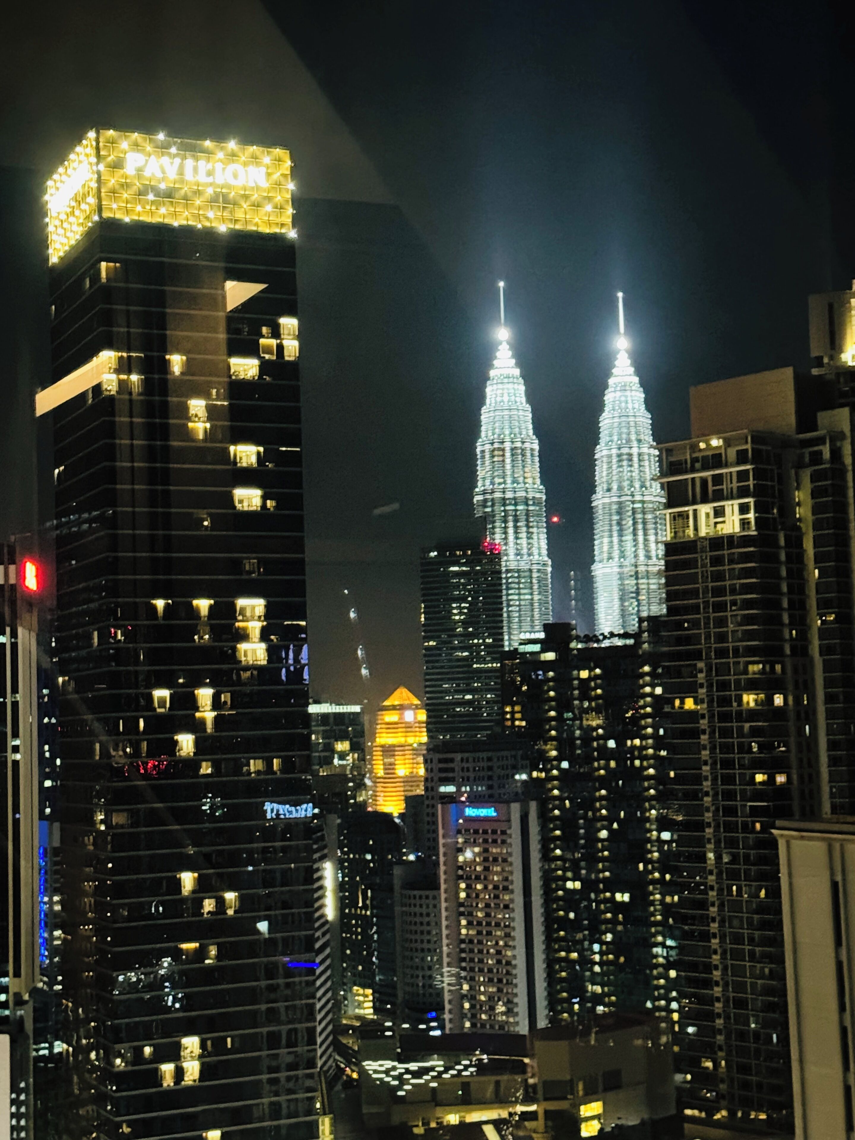 A cityscape at night with illuminated skyscrapers, including the iconic twin towers.