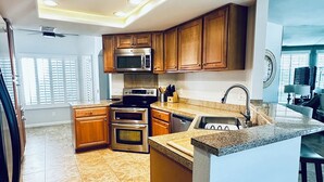 A modern kitchen with wooden cabinets, stainless steel appliances, a granite countertop, and a built-in island with bar stools.