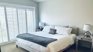 A bedroom with a bed, a ceiling fan, a nightstand, a lamp, and a window with blinds.