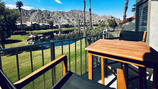 A balcony with a view of a lake, palm trees, and a mountain range.