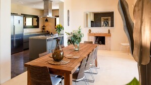 A modern kitchen with a central island, a dining area with a wooden table and chairs, and a fireplace. - Stunning Villa With Gardens (Sant Josep de sa Talaia)