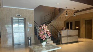 A hotel lobby with a reception desk, a staircase, and a trash can. - Arabia Style Homy Murni (Medan)