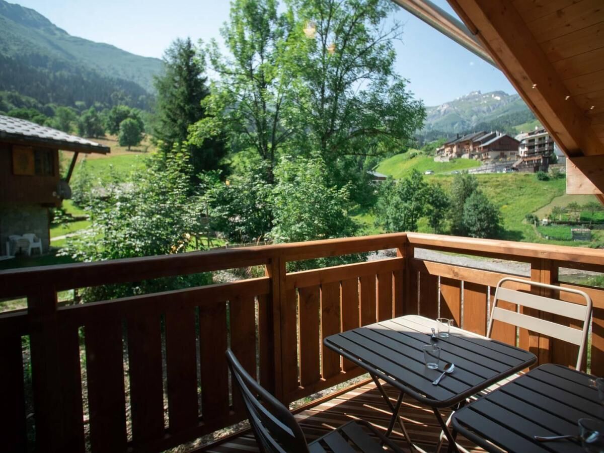 A wooden deck with a table and chairs, overlooking a lush green valley and distant buildings.