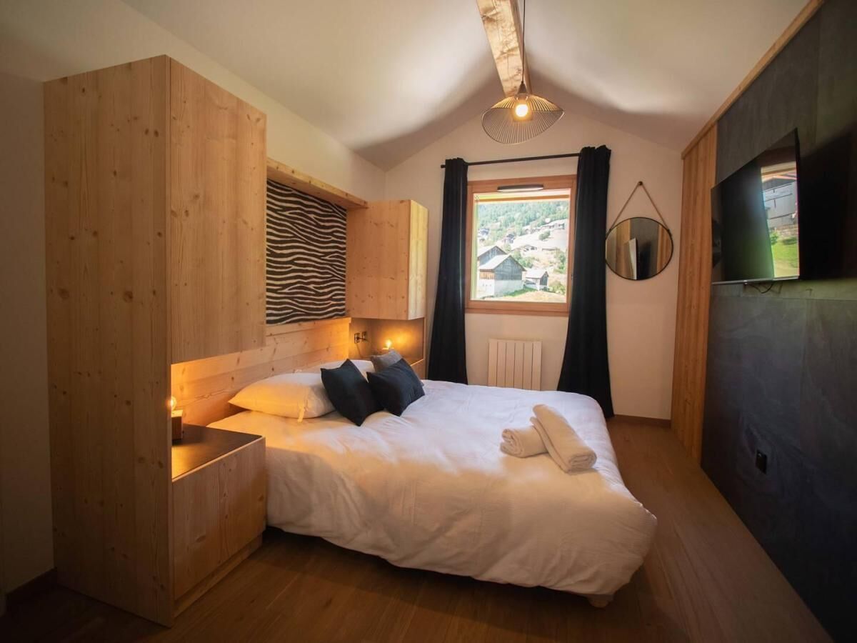Un dormitorio con cabecera de madera, cama con ropa de cama blanca, mesita de noche, espejo y ventana con cortinas.