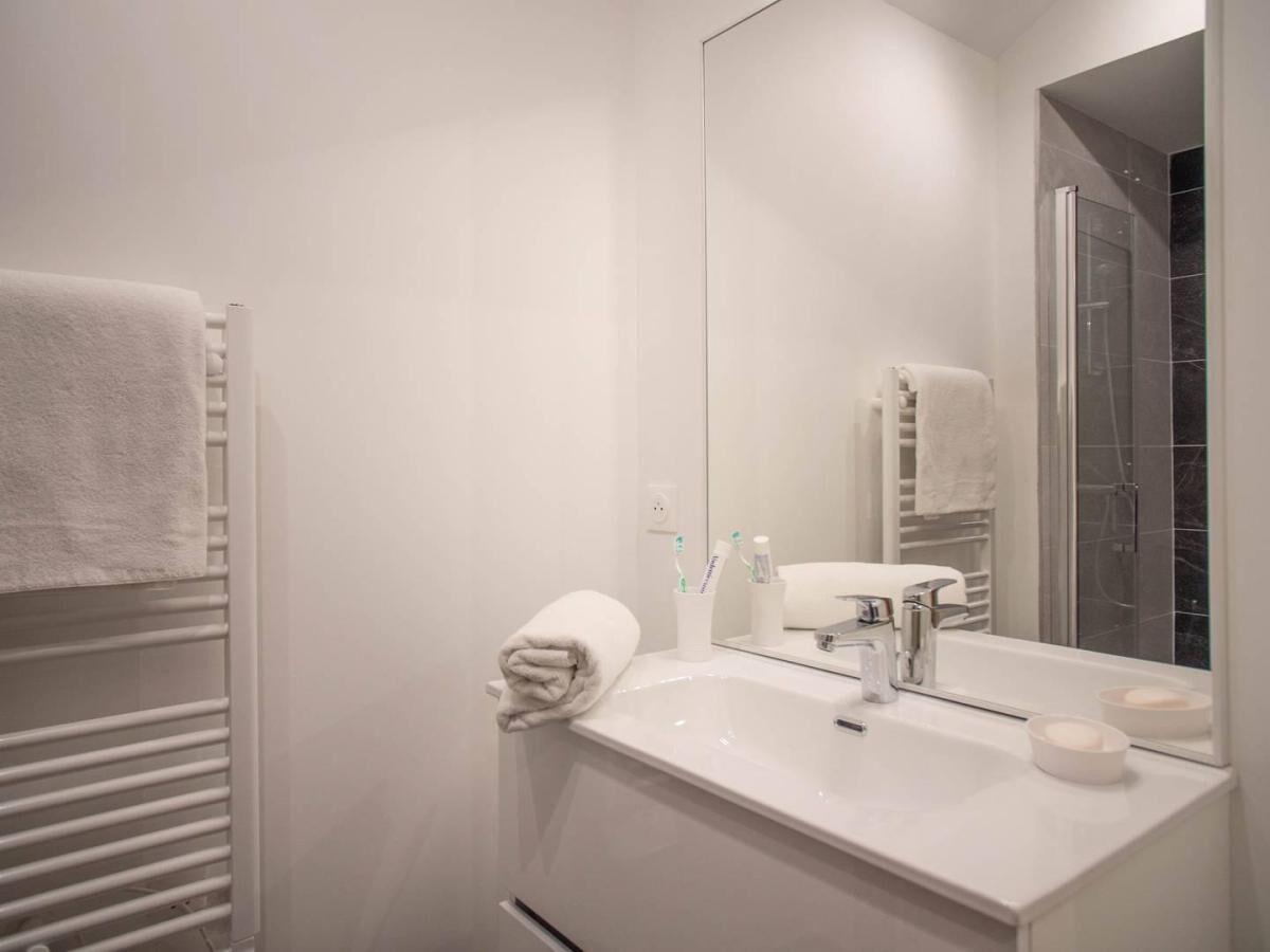 Un baño moderno con lavamanos, espejo y toallero blancos.
