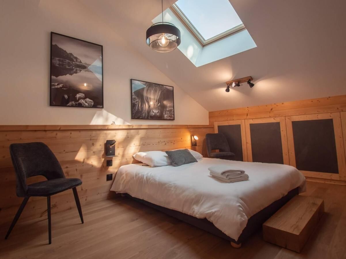 Ein Schlafzimmer mit Dachfenster, Holzwänden, einem Bett mit Kissen, einem Sessel und Kunstwerken an der Wand.
