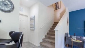 Un intérieur moderne avec un escalier, un coin repas doté d’une chaise noire et un mur d’accent bleu.