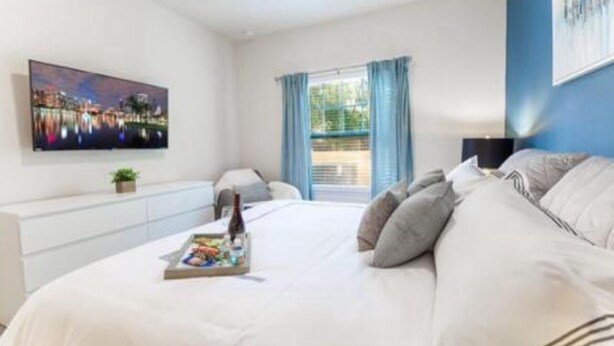 Une chambre d’hôtel avec un grand lit, une table de chevet, un téléviseur fixé au mur et une fenêtre avec des rideaux.