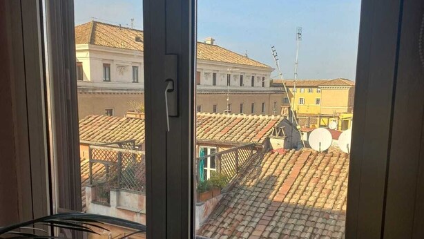 Une vue depuis une fenêtre, avec un garde-corps de balcon en métal, donnant sur un quartier résidentiel avec des toits recouverts de tuiles en terre cuite et des bâtiments dotés de balcons.