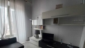 Un salon moderne avec un canapé, un téléviseur à écran plat, une lampe et une bibliothèque.