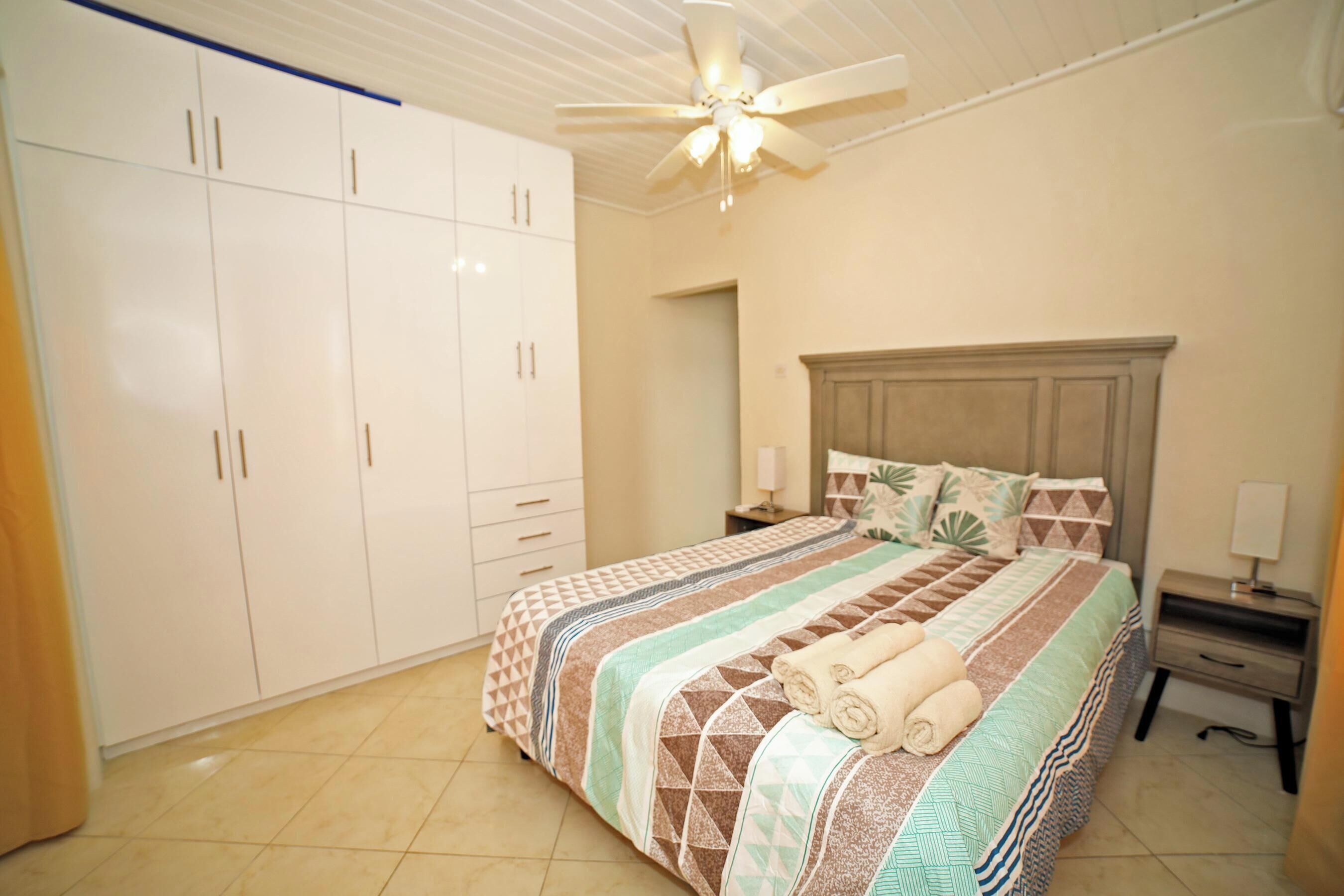 Une chambre à coucher comprenant un lit, des tables de chevet, une armoire et un ventilateur de plafond.