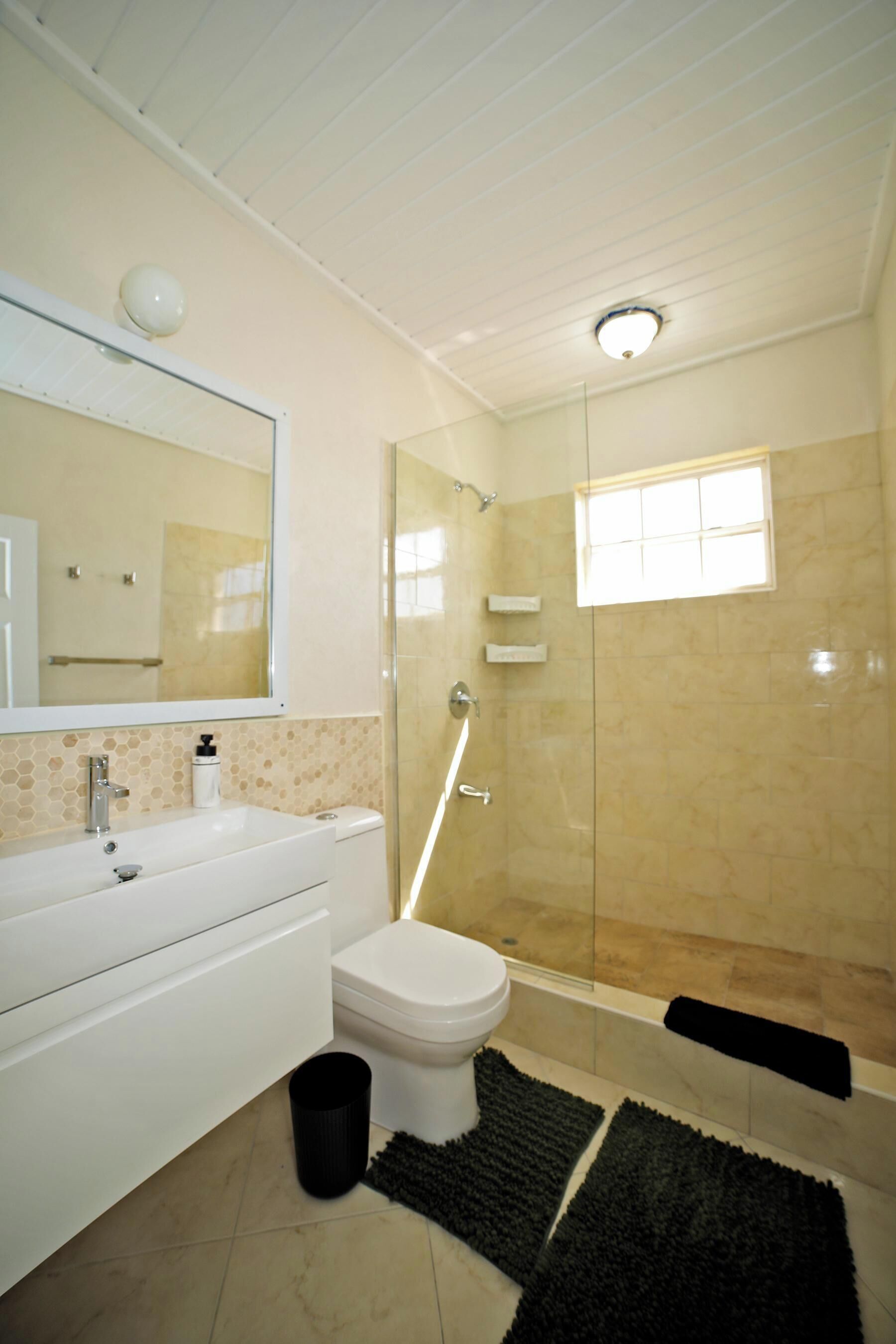 A bathroom with a white sink, a toilet, a glass shower enclosure, and a small window.