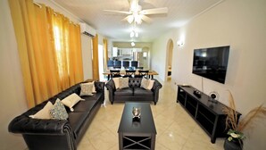 Un salón con un sofá de cuero negro, una mesa de centro y un televisor sobre un mueble.