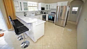 Cocina moderna con armarios blancos, electrodomésticos de acero inoxidable y una isla central con taburetes de bar.