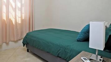Een slaapkamer met een bed, een nachtkastje met een afstandsbediening, een airconditioner en een raam met gordijnen.