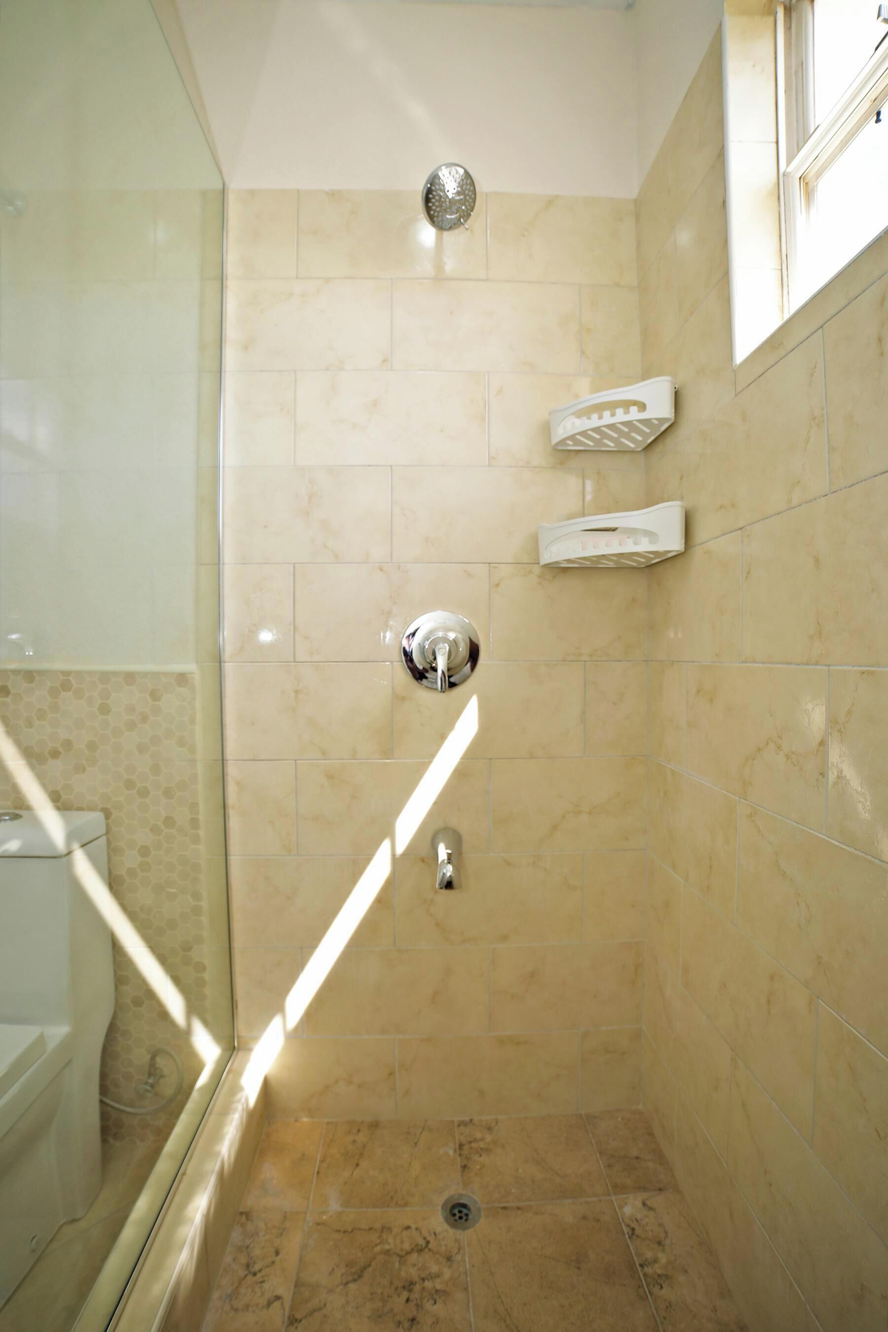 Um pequeno banheiro com azulejos, porta de vidro, chuveiro e painel de controle.