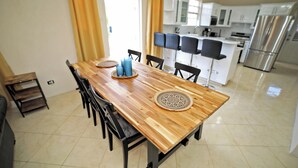 Una cocina moderna con armarios blancos, un refrigerador de acero inoxidable y un comedor con mesa de madera y sillas negras.