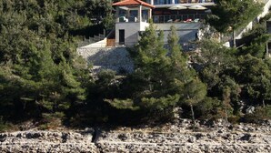 A coastal property with a modern building, a small pavilion, and a rocky shoreline.