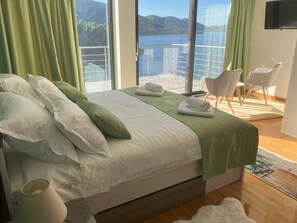 Enjoy a serene view of the water and mountains from the comfort of this spacious room, featuring a large bed and stylish seating area.