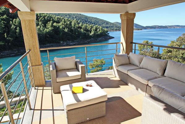 Relax in a serene outdoor space with a sofa, chaise lounge, and ottoman, overlooking a body of water and forested hillside.