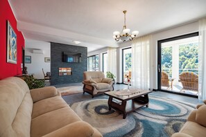 A modern living room with a sofa, armchair, and coffee table, a fireplace, and a balcony with outdoor seating.