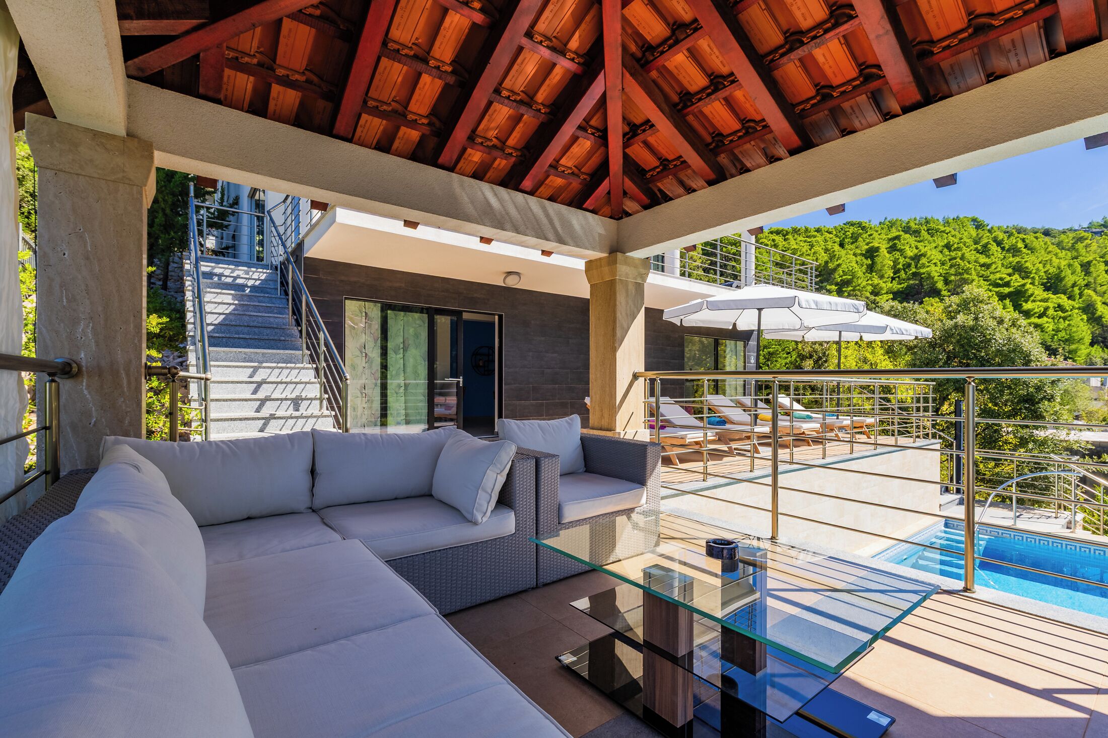 Un espacio exterior moderno con una mesa de vidrio, un sofá blanco y un área de descanso junto a la piscina.