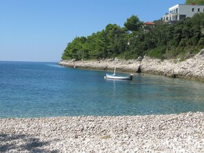 Enjoy a serene coastal retreat with a boat moored on the pebbly beach, surrounded by lush greenery and a nearby cliff.