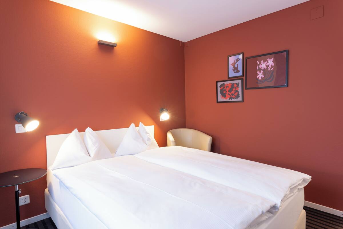 A hotel room with a bed, two wall-mounted lamps, and two framed pictures.