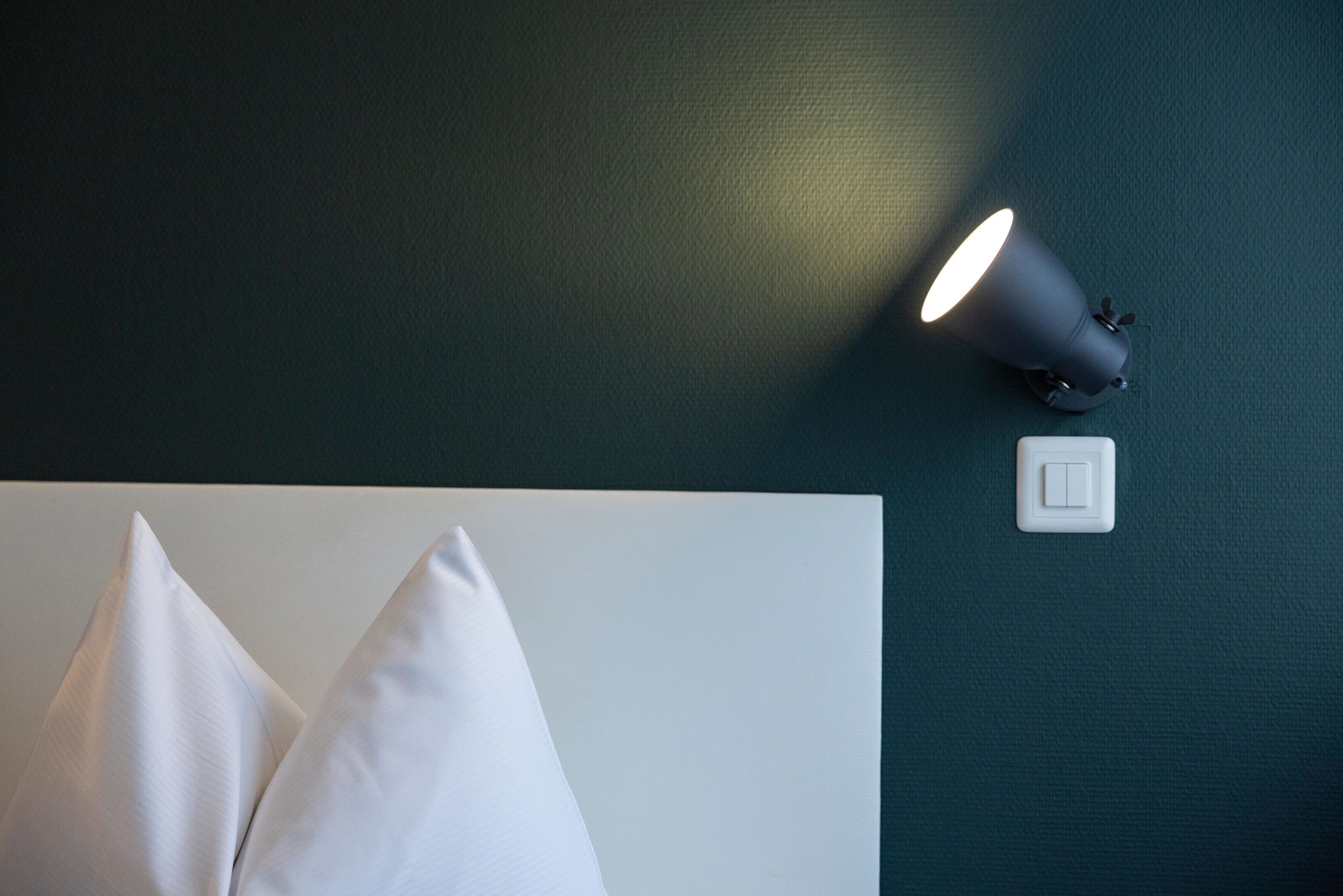 Un letto con cuscini bianchi e una lampada fissata al muro.