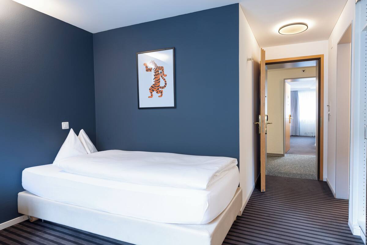 A hotel room with a bed, a framed picture on the wall, and a hallway leading to another room.