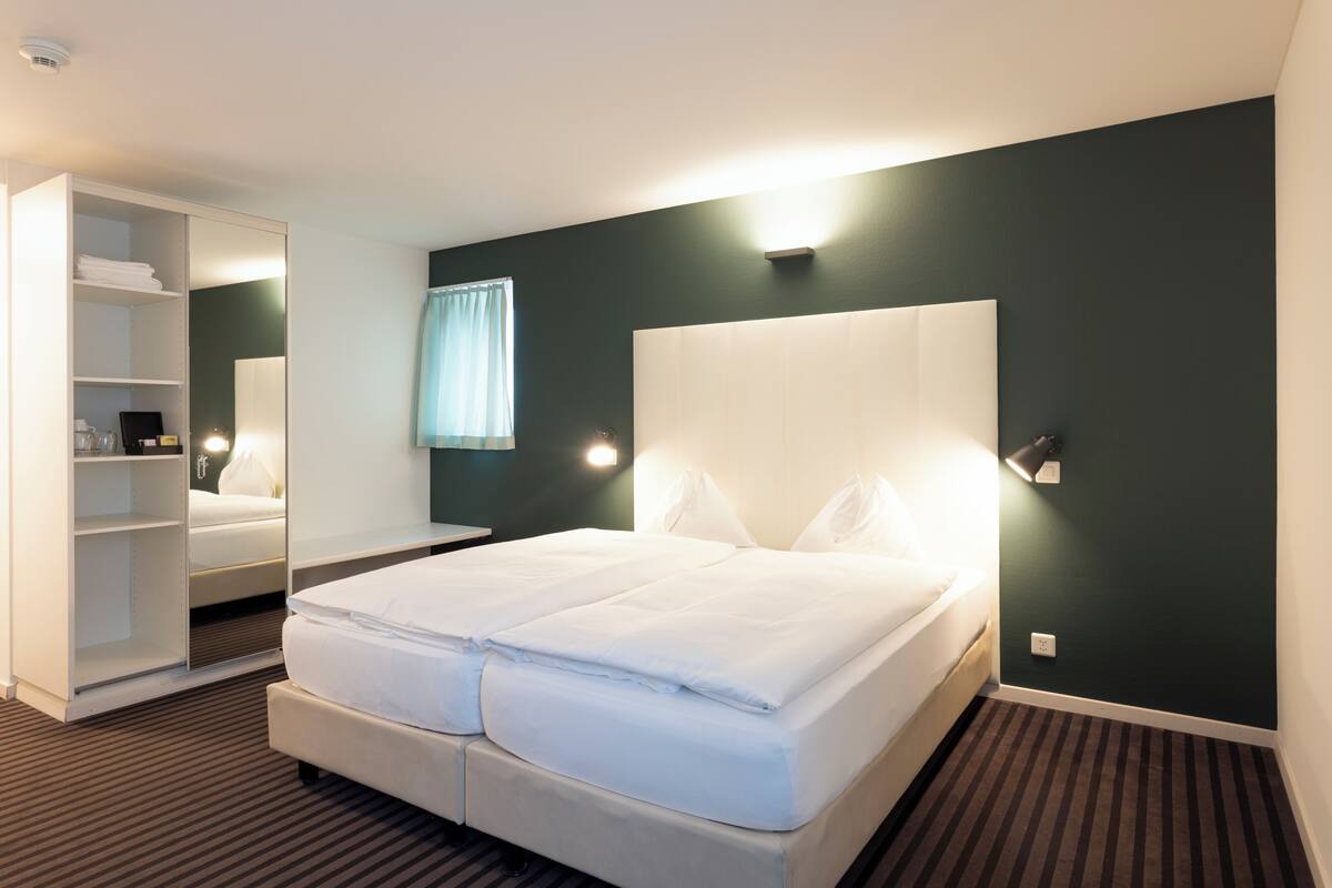 A hotel room with a large bed, a wardrobe, a mirror, and a nightstand.