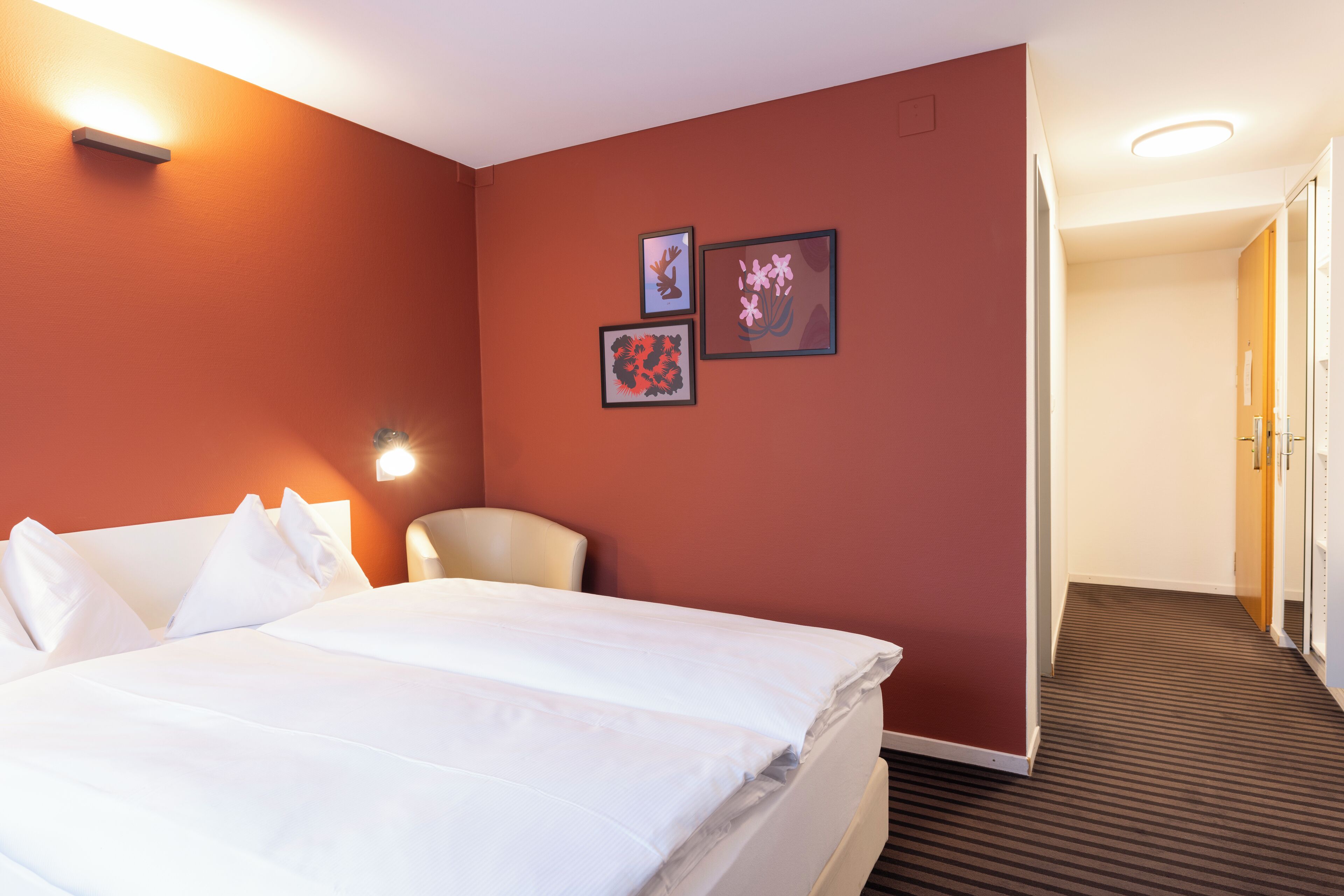 Ein Hotelzimmer mit einem Bett, einem Sessel und drei gerahmten Bildern an der Wand.