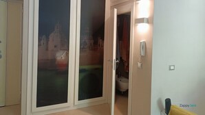 A room with a sliding door leading to a balcony with a view of a building. There is a bedside table with a lamp and a telephone on the wall. - St. Peter's  (Roma)