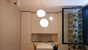 A compact kitchen with a central island, pendant lighting, and a view of a patterned wall. - St. Peter's  (Roma)