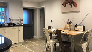 A modern kitchen with white cabinets, a dark door, and a dining area with a wooden table and chairs. - Idyllic cottage with private hot tub in picturesque village in the Peak District (Brassington, Matlock)