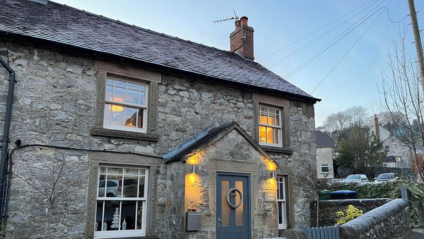 A stone cottage with a dark blue door, a small porch, and a wreath hanging on the door. - Idyllic cottage with private hot tub in picturesque village in the Peak District (Brassington, Matlock)