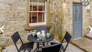 A stone building with a round table and four chairs, a window, and a door. - Idyllic cottage with private hot tub in picturesque village in the Peak District (Brassington, Matlock)