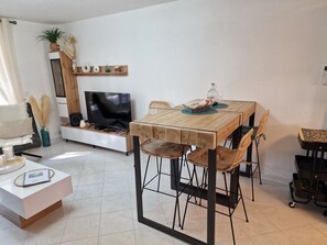 Un salon moderne avec une table à manger en bois, des chaises en osier, un téléviseur à écran plat et un canapé blanc.