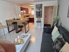 Un salon moderne avec un canapé gris foncé, une table basse décorée de bougies et un coin repas avec des chaises en osier.