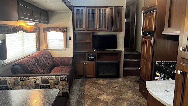 A compact RV kitchen with a dining area, a built-in TV, and a fireplace. - Spacious Lakeside Travel Trailer: Ultimate Comfort Awaits (Bridgeport)