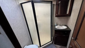 A compact bathroom with a shower enclosure, a toilet, a sink, and a mirror. - Spacious Lakeside Travel Trailer: Ultimate Comfort Awaits (Bridgeport)